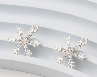 May include: Two silver snowflake charms with clear rhinestone accents. The charms have a loop at the top for attaching to jewelry or other crafts.