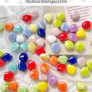May include: A collection of colorful ceramic shell beads in various shades of red, orange, yellow, green, blue, white, and pink. The beads are scattered on a white surface. The text "Medusa Boutique Store" is visible at the top.