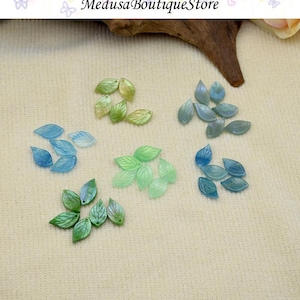 Puede incluir: Conjunto de cuentas en forma de hoja en tonos verdes y azules. Las cuentas translúcidas tienen un brillo sutil y vetas detalladas. La imagen incluye el texto "Medusa Boutique Store".