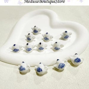 May include: A collection of miniature white ceramic teapots with blue floral designs. The teapots are arranged on a white heart-shaped tray. The text "Medusa Boutique Store" is at the top of the image.