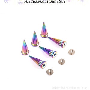 Peut inclure: Un ensemble de six clous métalliques en forme de cône irisés avec un dos à visser. Les clous sont un arc-en-ciel de couleurs, y compris le violet, le bleu, le vert et le rose. Les clous sont parfaits pour ajouter une touche punk rock ou gothique aux vêtements, sacs ou chaussures.