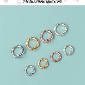 May include: Assortment of silver, gold, and rose gold jump rings. The jump rings are different sizes and are arranged on a light blue background.