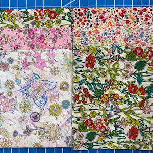 May include: A collection of floral patterned fabric squares in various colors. The fabrics feature designs with pink, red, yellow, and blue flowers and foliage on a white background. The squares are arranged on a blue grid.