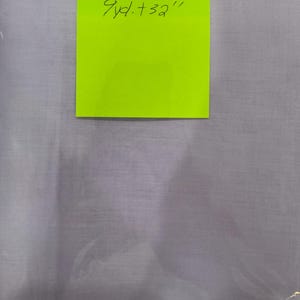 May include: A light purple fabric, possibly a textile or material, is shown in the image. A bright green sticky note is attached to the fabric, with the handwritten text "9yd. + 32"" in black ink. The fabric appears to be folded or draped.