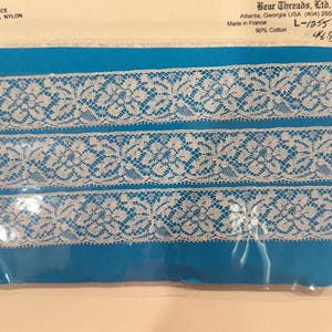 May include: White floral lace ribbon on a blue background, packaged in plastic. The label indicates it's made in France with 90% cotton and 10% nylon. The label also includes the text "Bear Threads, Ltd."