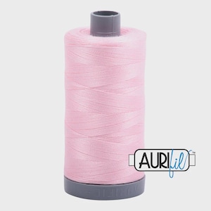 May include: A spool of light pink thread, ideal for sewing and quilting projects. The thread is tightly wound on a gray spool with the brand name "Aurifil" printed on the side. The thread is a soft, pastel color.