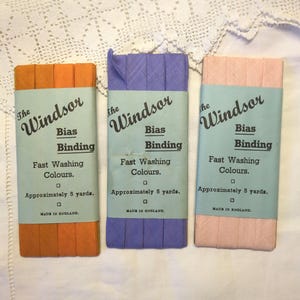 May include: Three packages of bias binding in orange, purple, and pink. Each package has the text "The Windsor Bias Binding Fast Washing Colours. Approximately 5 yards. Made in England."