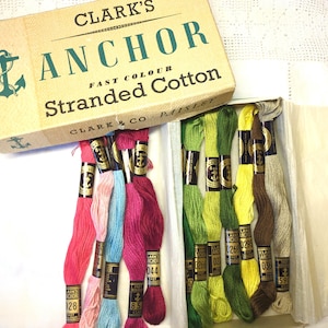 May include: A box of Clark's Anchor Fast Colour Stranded Cotton embroidery floss. The box is brown with a green anchor and the text "Clark's Anchor Fast Colour Stranded Cotton" printed on it. The box contains 10 skeins of floss in various colors, including pink, red, blue, green, yellow, and brown.