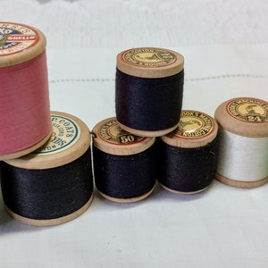 May include: An assortment of spools of thread in various colours, including green, pink, white, and black. The spools are labelled with the brand name "Sylko" and the text "Three Coats Silk Substitute Machine 40".