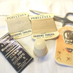 May include: Two spools of beige Peri-Lusta darning thread, a needle threader, a thimble, and a small box of needles. The thread spools are labeled "Fine Darning Thread, Made in England". The needle threader is labeled "Needle Threader". The box of needles is labeled "H. Milward & Sons Registered Needle Case Bevil Eyed Sharps No. 8 Made at Redditch, England."