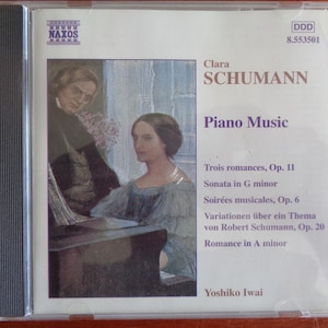 May include: A CD case featuring a portrait of Clara Schumann and the text "Piano Music." The cover includes the names of musical pieces and the artist, Yoshiko Iwai. The CD is in a clear plastic case.