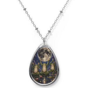 Può includere: Collana color argento con un ciondolo raffigurante tre rane verdi in posa yoga, che tengono una luna piena contro un cielo stellato. Il ciondolo è di forma ovale.
