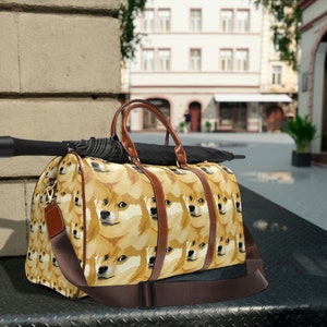 Könnte beinhalten: Eine braune Ledertasche mit einem Muster aus Shiba Inu-Hundegesichtern. Die Tasche hat einen braunen Lederriemen und ein schwarzer Regenschirm liegt auf der Tasche.