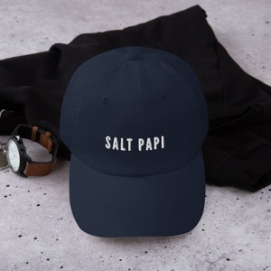 May include: A navy blue baseball cap with white embroidered text that reads "SALT PAPI".