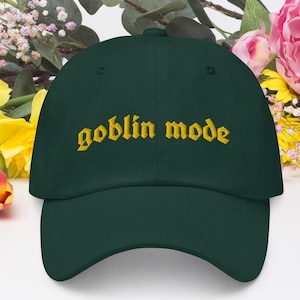 May include: A dark green baseball cap with the words "goblin mode" embroidered in gold.