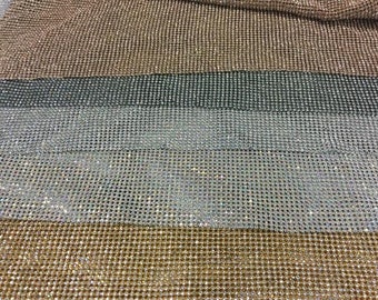May include: A close-up of a fabric with a sparkly, iridescent finish. The fabric is made of a mesh material and has a repeating pattern of small, round rhinestones. The fabric is available in four colors: gold, silver, black, and rose gold.