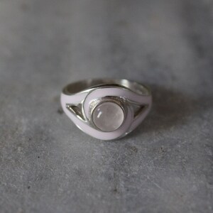 May include: A silver ring with a pink enamel band and a round, clear gemstone.