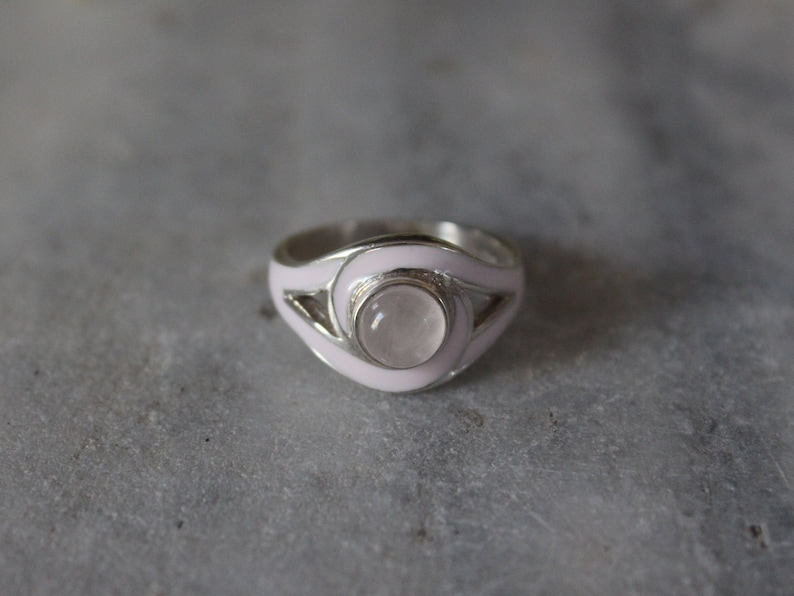 May include: A silver ring with a pink enamel band and a round, clear gemstone.