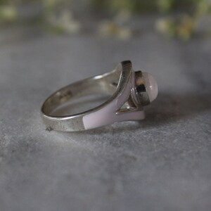 May include: A silver ring with a pink stone and white enamel accents.