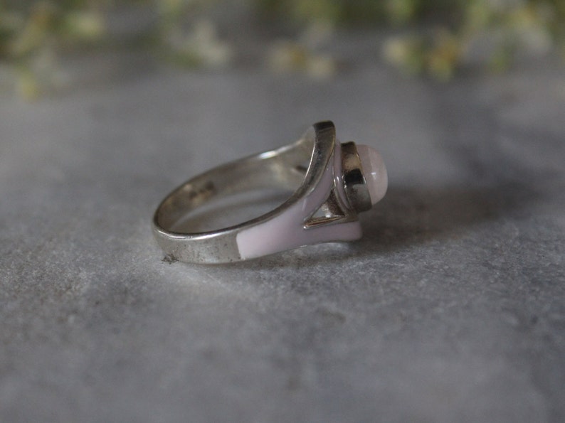 May include: A silver ring with a pink stone and white enamel accents.