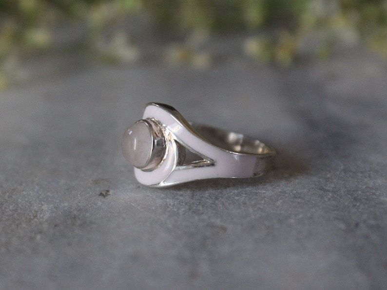May include: A silver ring with a pink enamel design and a pale pink gemstone in the center.