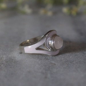 May include: A silver ring with a pink enamel design and a round, clear gemstone.