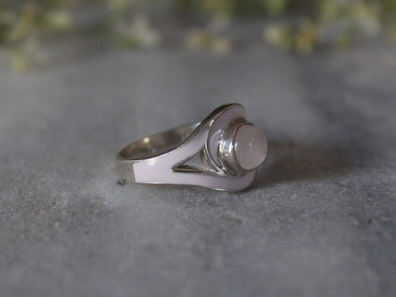 May include: A silver ring with a pink enamel design and a round, clear gemstone.