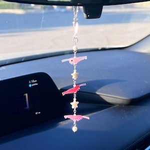 Puede incluir: Un adorno colgante para coche con una cadena de tono plateado, tres dijes de camarones rosas translúcidos, dos pequeñas cuentas blancas en forma de estrella y tres cuentas blancas redondas, suspendido de un cierre y cadena de metal.