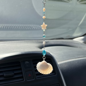 May include: A white seashell car charm with blue and white beads and a white star charm hanging from a silver chain.