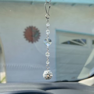 May include: A crystal car charm with a heart and a disco ball hanging from a silver hook.
