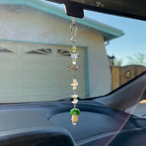 May include: A car charm with a green and white mushroom, a dragonfly, and white butterflies hanging from a silver chain.