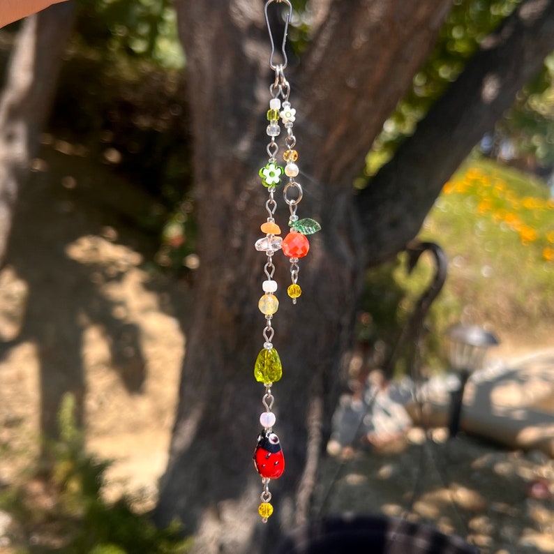 Pu&ograve; includere: Un braccialetto con ciondoli in argento con una variet&agrave; di perline colorate, tra cui verde, arancione, rosso e bianco. Le perline hanno la forma di fiori, foglie e una coccinella.