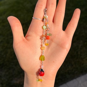 Pu&ograve; includere: Un braccialetto con ciondoli a catena d'argento con perline colorate, tra cui una coccinella, fiori e foglie.