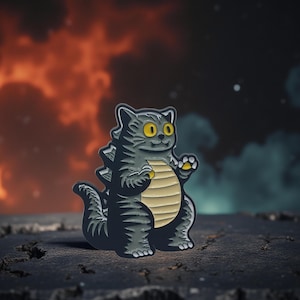 May include: A gray cat-shaped enamel pin with a Godzilla-inspired design. The pin features a yellow belly, yellow eyes, and a smiling expression. The background shows an orange and blue smoky effect.