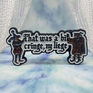 Könnte beinhalten: Ein schwarz-weißer Anstecker mit dem Text "That was a bit cringe, my liege". Der Anstecker zeigt Illustrationen von zwei mittelalterlichen Figuren. Eine Figur ist in Rot und Schwarz gekleidet, die andere in Braun.