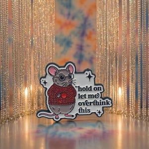 Könnte beinhalten: Ein skurriler Emaille-Pin mit einer Cartoon-Maus, die eine Brille und einen roten Pullover trägt und eine Tasse hält. Der Pin trägt den weißen Schriftzug "hold on let me overthink this". Der Pin hat einen weißen Rand mit Sternakzenten.