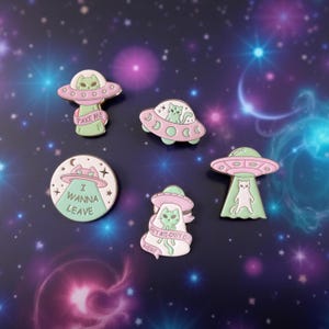 Könnte beinhalten: Eine Sammlung von Emaille-Anstecknadeln mit Katzen-Alien-Designs. Die Anstecknadeln zeigen fliegende Untertassen und Katzen in verschiedenen Posen, mit Sätzen wie "Take Me" und "I Wanna Leave". Die Farbpalette umfasst Rosa, Grün und Weiß.