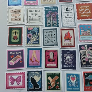 Könnte beinhalten: Eine Sammlung dekorativer Aufkleber mit verschiedenen Designs und Texten. Die Aufkleber zeigen Illustrationen von Skeletten, Blumen, Herzen und Texten wie "Enemies to Lovers" und "Slow Burn". Die Farbpalette umfasst Rosa, Blau und Lila.