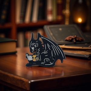 Könnte beinhalten: Schwarze Drachenfigur mit weißen Akzenten, die ein Buch liest. Ein kleiner goldener Drache befindet sich auf dem Buch. Die Figur steht auf einer Holzoberfläche, mit einem verschwommenen Hintergrund aus Büchern und gedämpftem Licht.