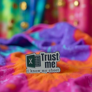Può includere: Spilla in smalto color argento con la scritta "Trust me I know my sheet". La spilla presenta un'icona verde del foglio di calcolo Excel con una "X" bianca e una griglia. La spilla è posta su uno sfondo colorato e fantasia.