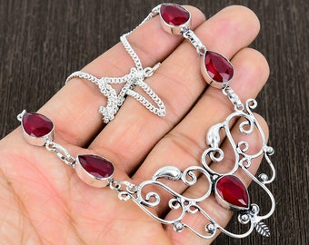 May include: A silver necklace with a delicate, ornate design features five red gemstone drops. The necklace has a chain closure.