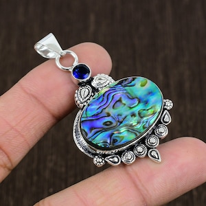 Könnte beinhalten: Ein silberner Anhänger mit einem blauen Edelstein und einer ovalen Einlage aus Abalone-Schale. Der Anhänger hat ein detailliertes Design mit aufwendiger Silberarbeit.