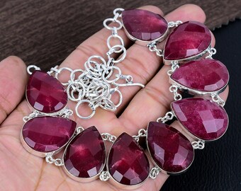 May include: A silver necklace with a chain and nine teardrop-shaped red gemstones. The necklace is on a hand.