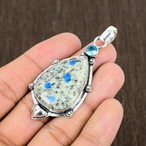 K&ouml;nnte beinhalten: Ein silberner Anh&auml;nger mit einem tropfenf&ouml;rmigen blau-wei&szlig;en Stein, der in einen silbernen Rahmen gefasst ist. Der Anh&auml;nger hat einen kleinen blauen Stein oben.