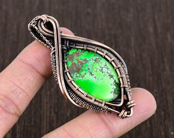 May include: A green turquoise stone pendant wrapped in copper wire. The pendant is shaped like a teardrop and has a delicate, intricate design.