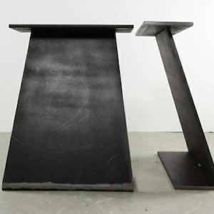 Könnte beinhalten: Zwei schwarze Metalltischbeine mit dreieckiger Form. Die Beine sind aus dickem Metall gefertigt und haben einen rustikalen, industriellen Look.