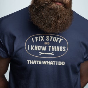 Peut inclure: Un t-shirt bleu marine avec un graphique ovale blanc vieilli qui dit "I fix stuff and I know things" avec un symbole de clé à molette. Le texte "That's what I do" est imprimé sous l'ovale.