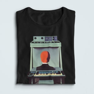 May include: A black t-shirt featuring a graphic of a person sitting in front of a synthesizer with a red head and a blue body.