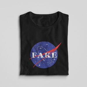 K&ouml;nnte beinhalten: Schwarzes T-Shirt mit einem blauen und roten NASA-Logo, auf dem in wei&szlig;en Buchstaben "FAKE" steht.