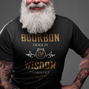 Può includere: Una maglietta nera con una grafica dorata che recita "Bourbon Goes In & Wisdom Comes Out".